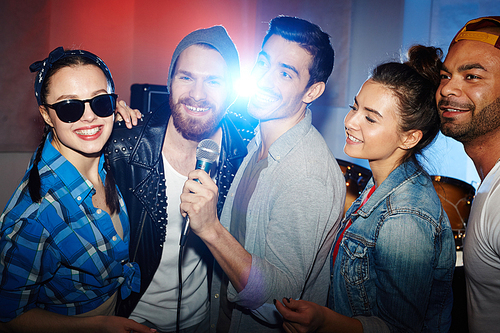 Group of smiling party people, men and women, having fun on stage singing to microphone at night club party