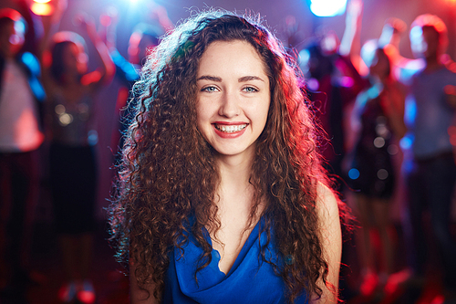Portrait of beautiful girl with long curly hair standing on dancing crowd background and  with bright toothy smile