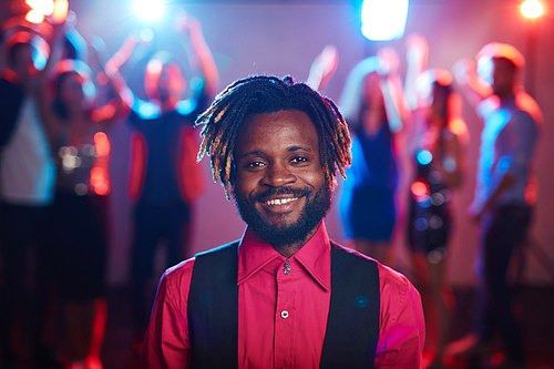 Waist-up portrait of attractive African-American with short dreadlocks smiling at camera cheerfully while hanging out in club