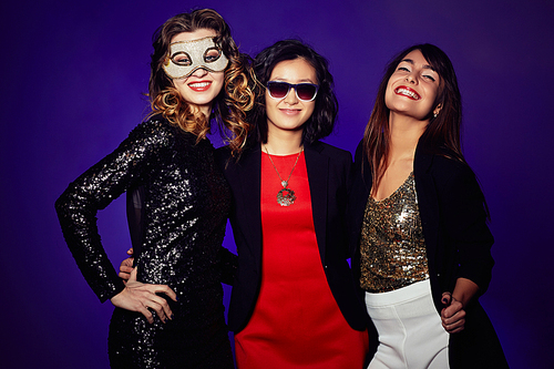 Three glamorous party goers standing against dark background and  with charming smiles, group portrait