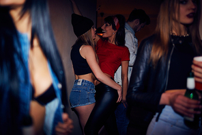 Sneak shot of crowded dark club, semi naked young people partying and drinking beer with two  beutiful girls dancing in background