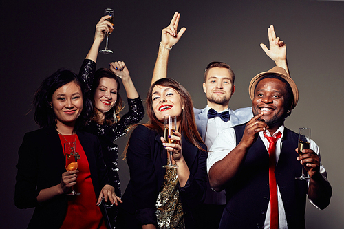 Group portrait of cheerful young people posing for photography with champagne flutes in hands while clubbing, dark background