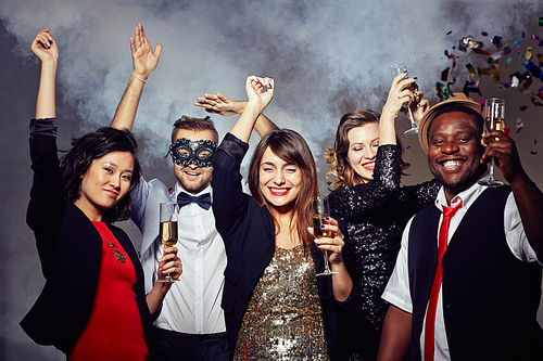 Celebrating New Year with friends: cheerful young people posing for photography while having fun in night club, smoke and colorful confetti on background