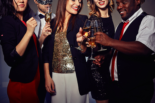Close-up shot of stylish young people toasting with champagne flutes while standing against dark background