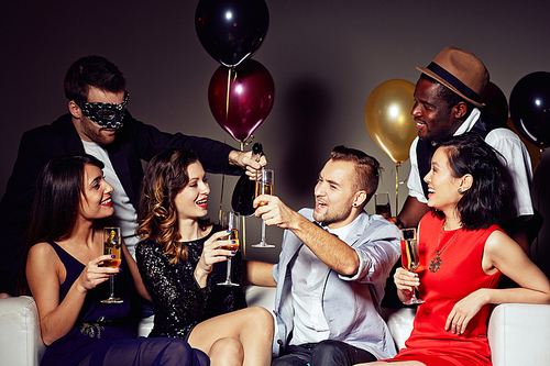 Multi-ethnic group of friends gathered together at home party and having fun, they holding champagne flutes in hands