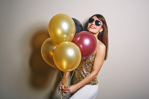 Waist-up portrait of beautiful young woman holding bunch of colorful balloons in hands and  with toothy smile, studio shot