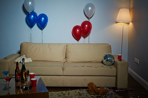 Empty room with couch, lamp, balloons, disco-ball, teddybears and drinks after party