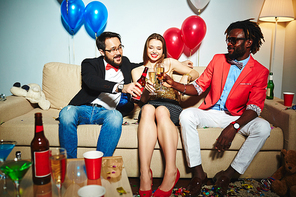 Two middle-aged men and one young woman sitting in living room decorated for New Year celebration and toasting with alcohol