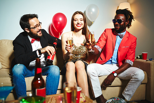 Attractive young woman with wide smile chatting and drinking alcohol with her male colleagues while having company party