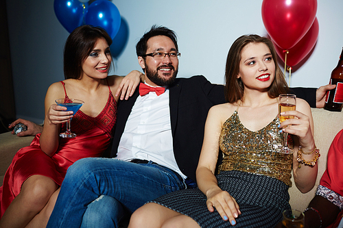 Male and female clubbers celebrating momentous event with alcohol: they sitting on couch and looking away joyfully