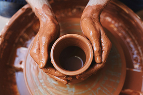 Dirty hands of potter on rotating clay jug