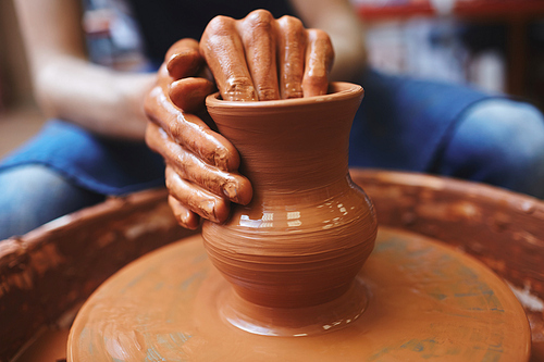 Human hands making curves of rotating clay jug