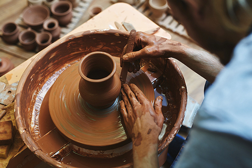 Rotating jug and hands of pottery master working with hand-tool