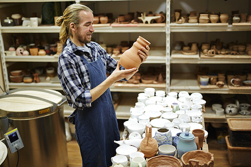 Happy potter looking at ceramic jug in his hands