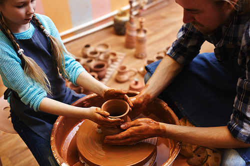 Craftsman and his daughter touching rotating jug in pottery-wheel