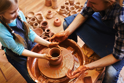 Little girl helping her father to make pots in his workshop
