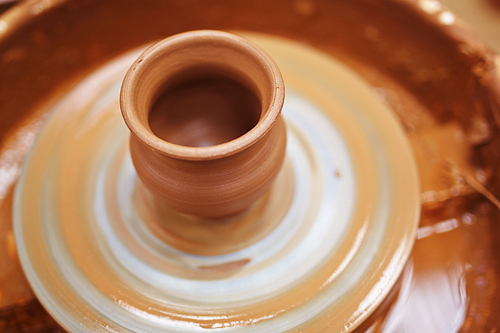 Unfinished jug rotating in pottery-wheel in workshop of craftsman
