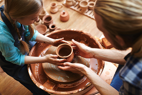 Top view of man and his daughter making jugs in pottery-wheel