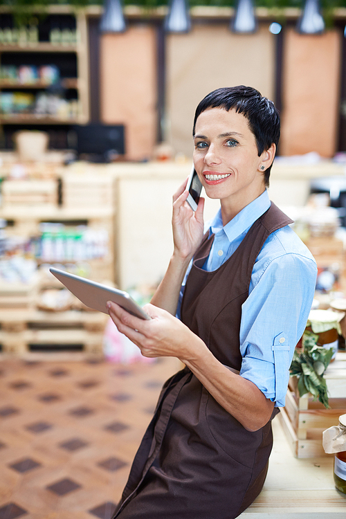 Portrait of beautiful shop owner checking online order details on mobile phone, lovely store of organic products on background