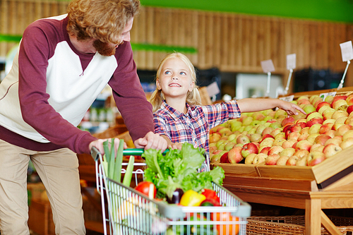 Little girl asking her father to take one of apples in supermarket