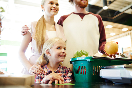 Happy family of three standing by cash-register in modern hypermarket