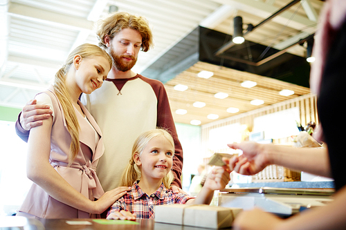 Little buyer giving plastic card to seller to pay for products with her parents near by