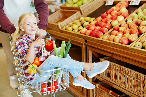 Little girl sitting in shopping cart with vegs and enjoying cart ride