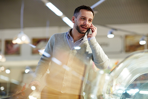 Portrait of handsome mature man doing grocery shopping in supermarket: calling his wife asking what to buy