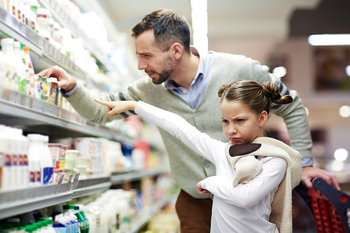 Capricious daughter asking her father to buy her tasty yoghurt in supermarket