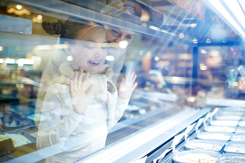 Excited girl looking at assortment of various ice-creams in showcase