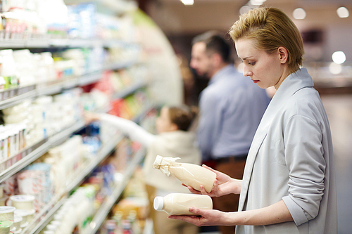 Side view portrait of blond woman choosing milk in dairy product department