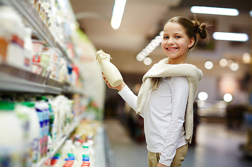Happy child with bottle of fresh milk standing by supermarket-shelf