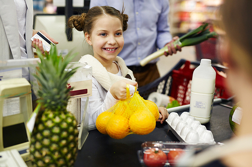 Happy girl giving oranges to cashier at supermarket checkout