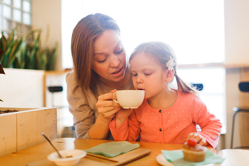 Young woman looking at her daughter drinking hot tea