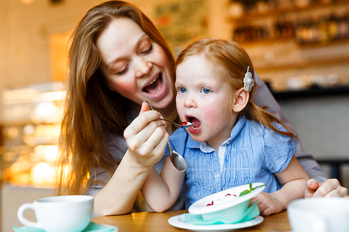 Woman feeding her daughter with sweet dessert