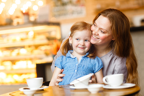 Young mother embracing her daughter in cafe