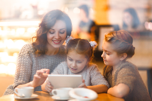 Twin sisters and their mother with touchpad sitting in cafe