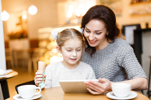Girl with ice-cream and her mother watching something online in touchpad