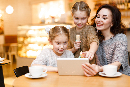 Twin girls and her mother watching online program in cafe