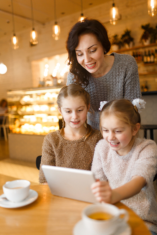 Modern young woman and her twin daughters with touchpad spending leisure in cafe