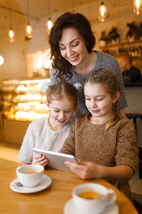 Woman and little girls with touchpad enjoying leisure in cafe