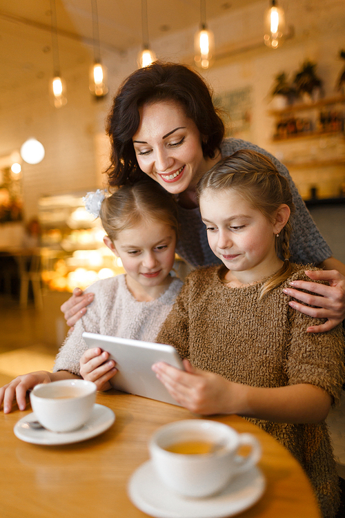 Young woman embracing her twin daughters with touchpad