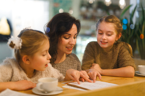 Young female and her daughters reading menu in cafe