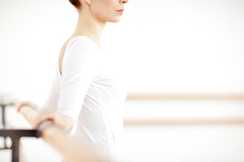 Mid-section of fit ballerina leaning at bar by her hands during class