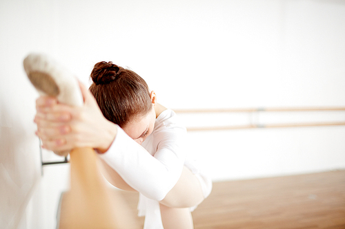 Ballerina keeping her feet on bar while practicing stretching in class