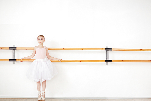 Little girl in ballet outfit standing by bars along wall of classroom