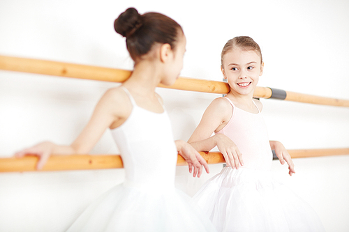Two little ballerinas leaning at bars and having talk after ballet classes
