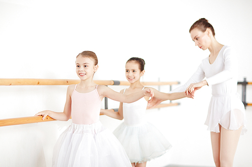 Ballet teacher holding her two learners by hands while repeating exercise in class