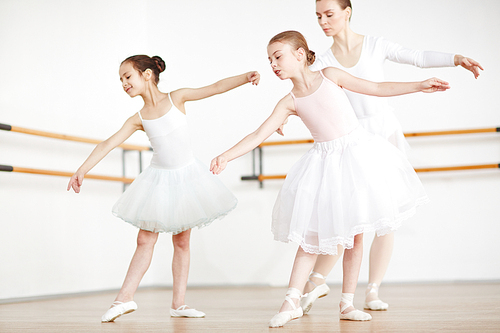 Two little girls leaning aside while repeating after their teacher during training