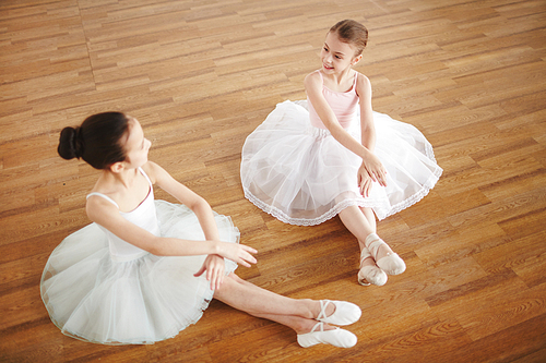 Cute little ballerinas in white shiffon skirts sitting on the floor and exercising